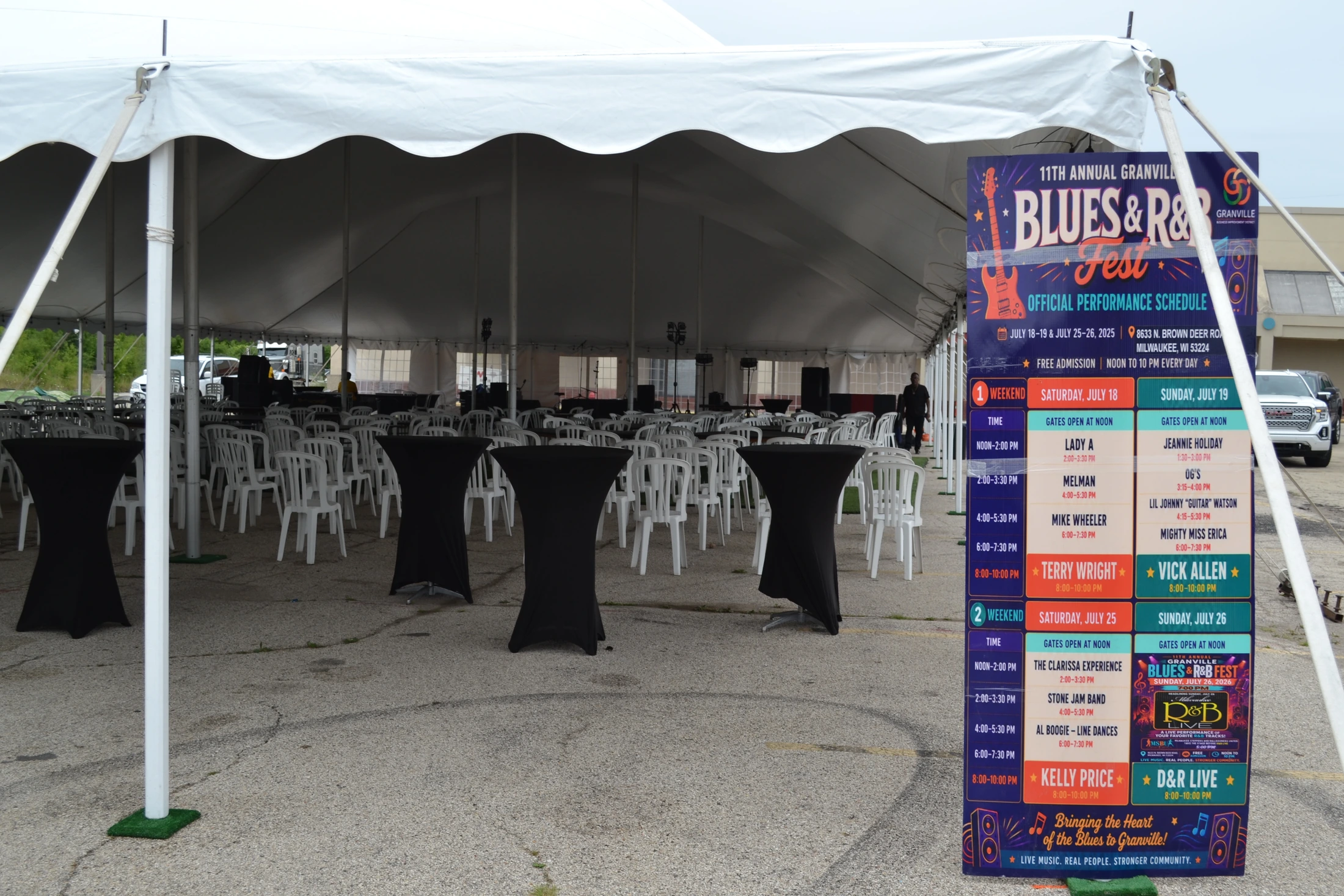 Large-format Granville performance schedule standing at the entrance to the festival tent beside guest seating